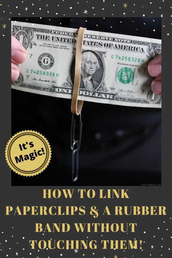 Holding a Dollar Bill with Rubber Band and Paperclips handing from it for magic trick.