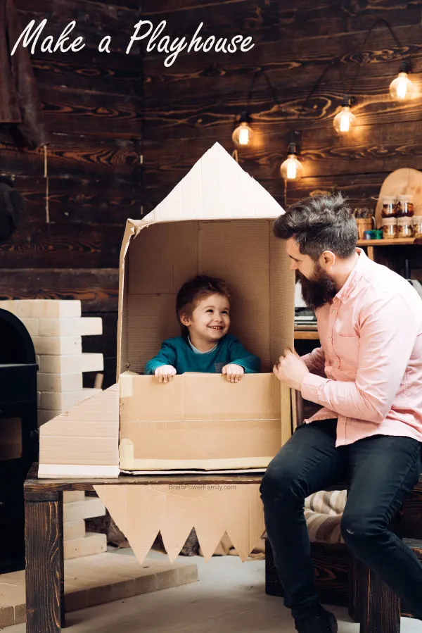 Dad making a cardboard playhouse rocket for child
